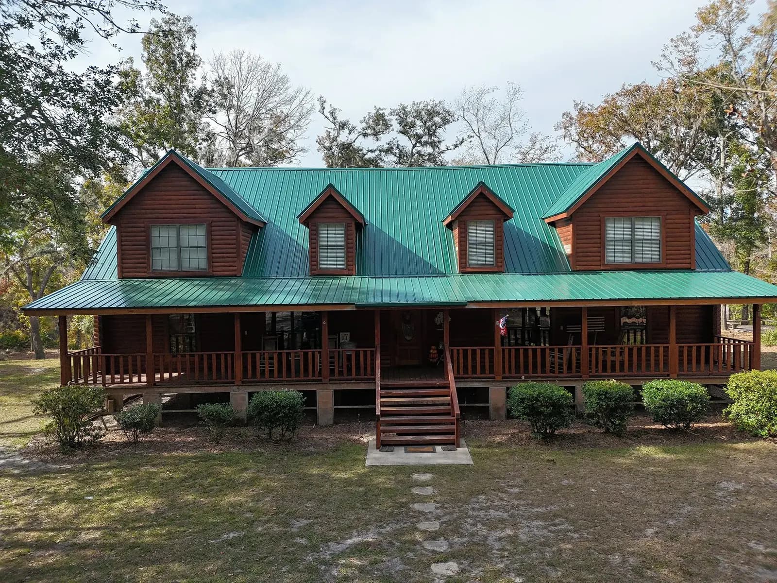 Front view of a log home with a completed teal metal roof