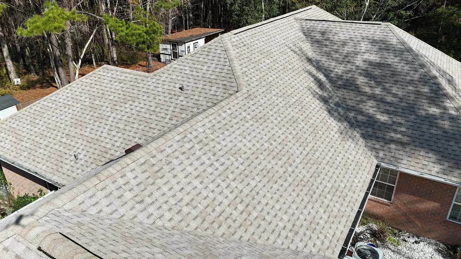 Aerial view of a completed light-gray shingle roof on a brick home